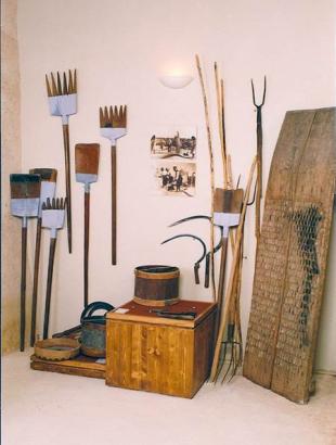 Γεωργικά σύνεργα. Ακουμπισμένα στον τοίχο, από αριστερά προς τα δεξιά, διακρίνονται τα σύνεργα του αλωνίσματος: ξυλόφτυαρα, θερνάτζια, δικράνια και η δουκάνη.